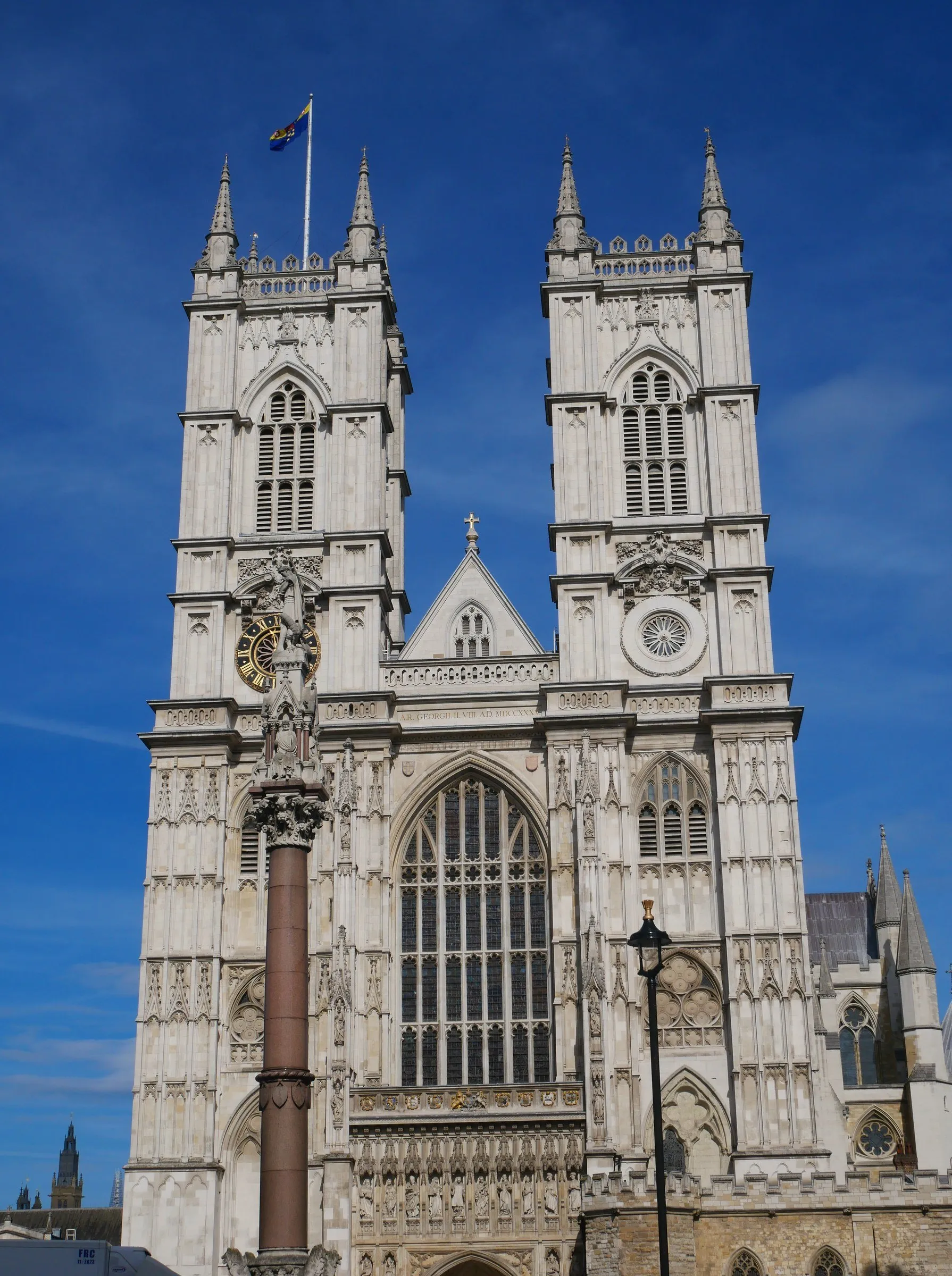 West front of Westminster Abbey with its two Gothic towers, seen from below against a deep blue sky.