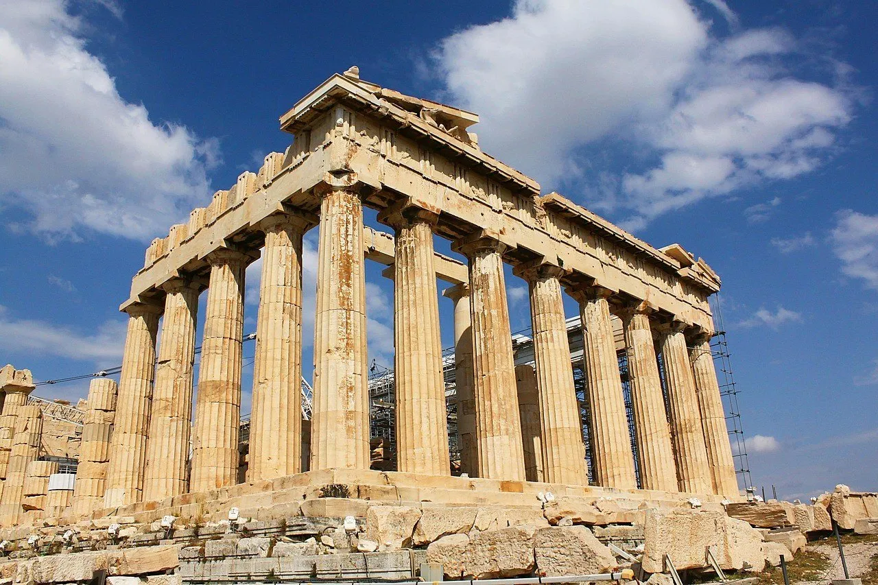Exterior of the Parthenon on the Acropolis of Athens, with marble columns under a blue sky with clouds.