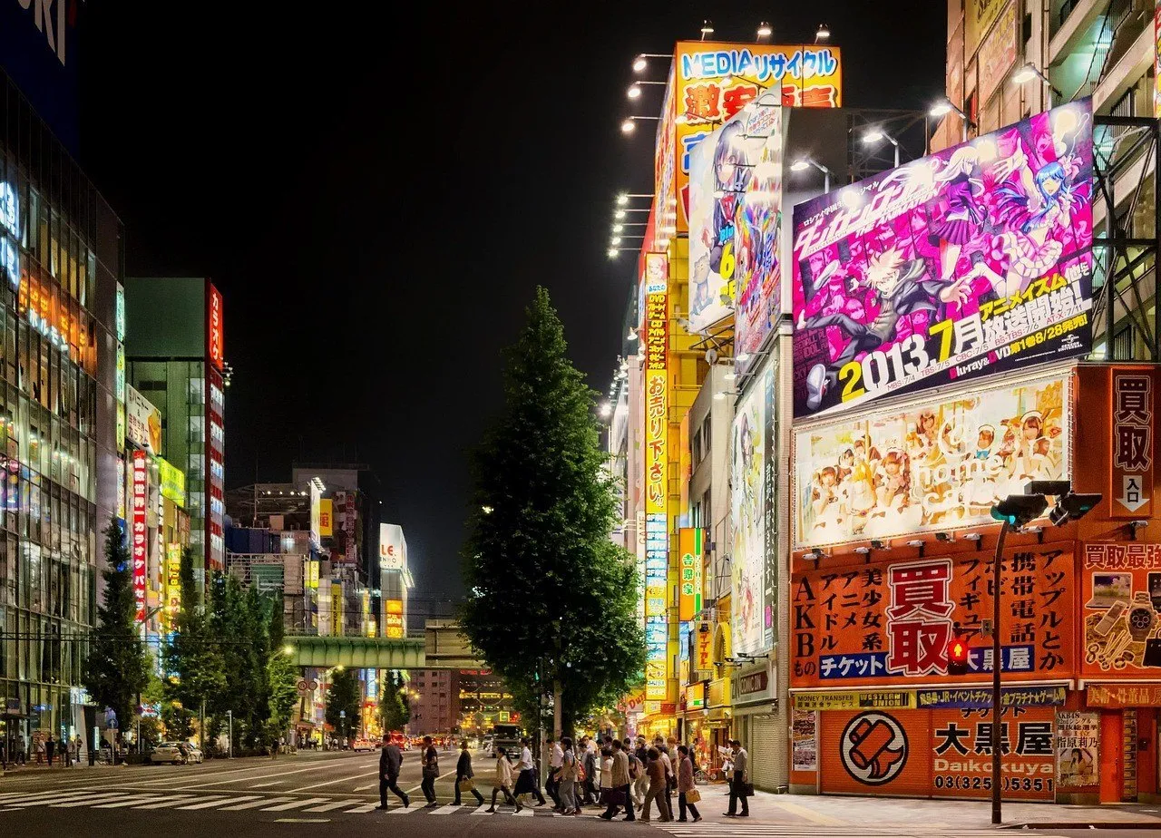 Calle de Akihabara de noche, con letreros luminosos, edificios comerciales y peatones cruzando.
