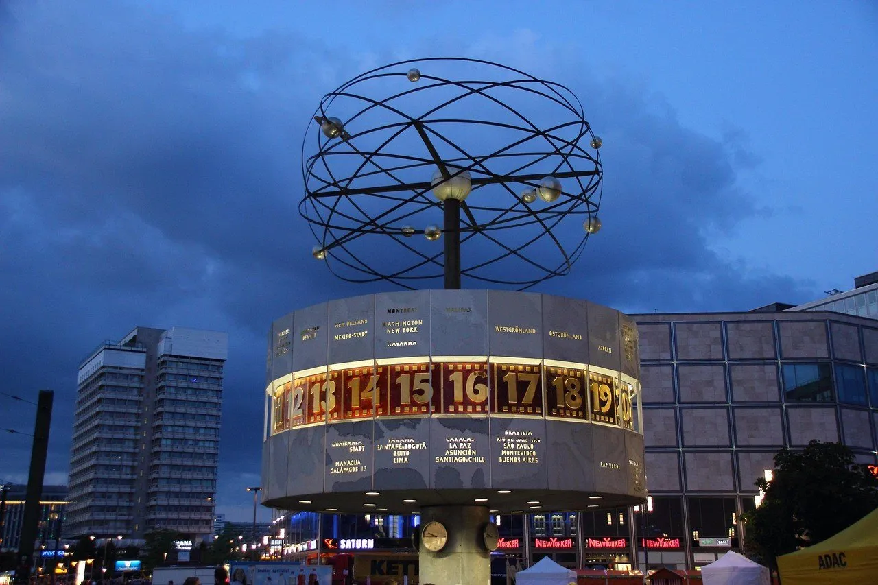 Relógio Mundial iluminado na Alexanderplatz, cercado por edifícios ao anoitecer.