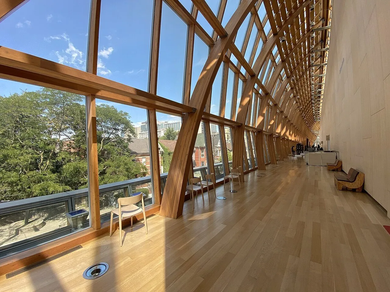 Corredor da Galleria Italia na AGO, com estrutura curva de madeira, grandes janelas e luz solar no piso.