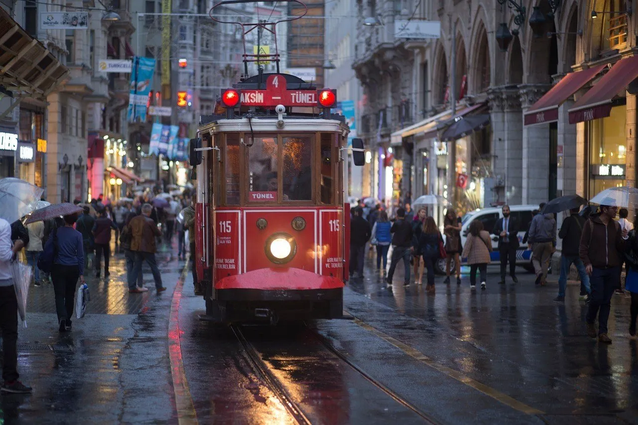 Tranvía rojo antiguo Taksim–Tünel en la Avenida İstiklal, con peatones con paraguas y adoquines mojados.