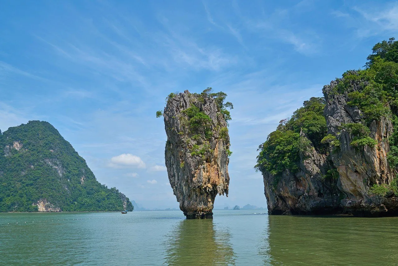 Rochedo de calcário Ko Tapu emergindo do mar na baía de Phang Nga, entre ilhas cobertas de mata, sob céu azul.