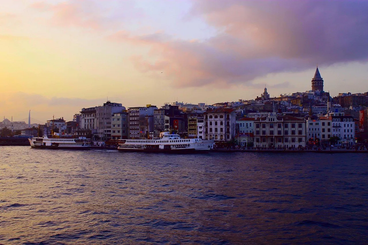 Ferris de pasajeros en el agua al atardecer, frente a las casas de Karaköy, con la Torre de Gálata al fondo y cielo violáceo.