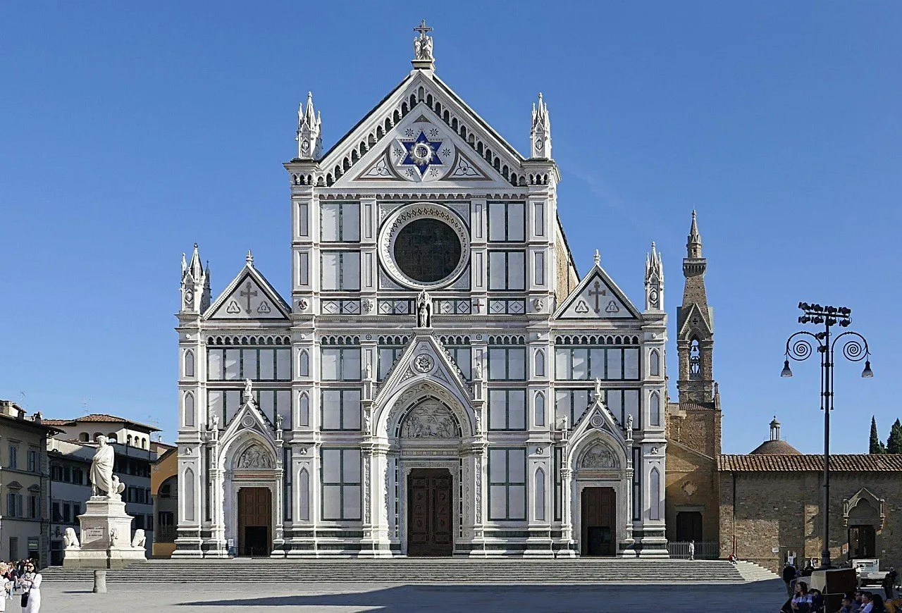 Marble facade of the Basilica of Santa Croce under a blue sky, with a statue of Dante on the left.