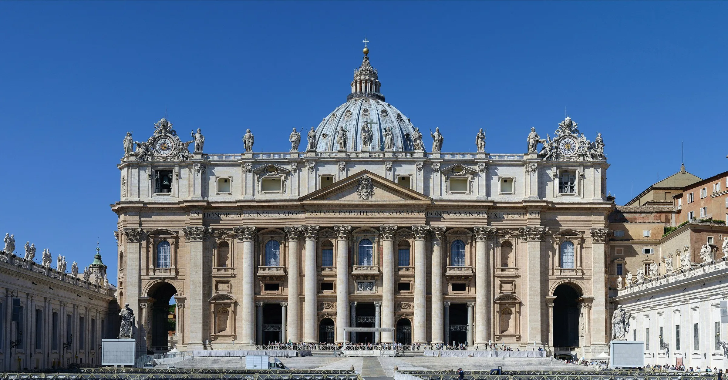 Facade of St. Peter's Basilica in the Vatican, with the dome at the center and a cloudless blue sky.