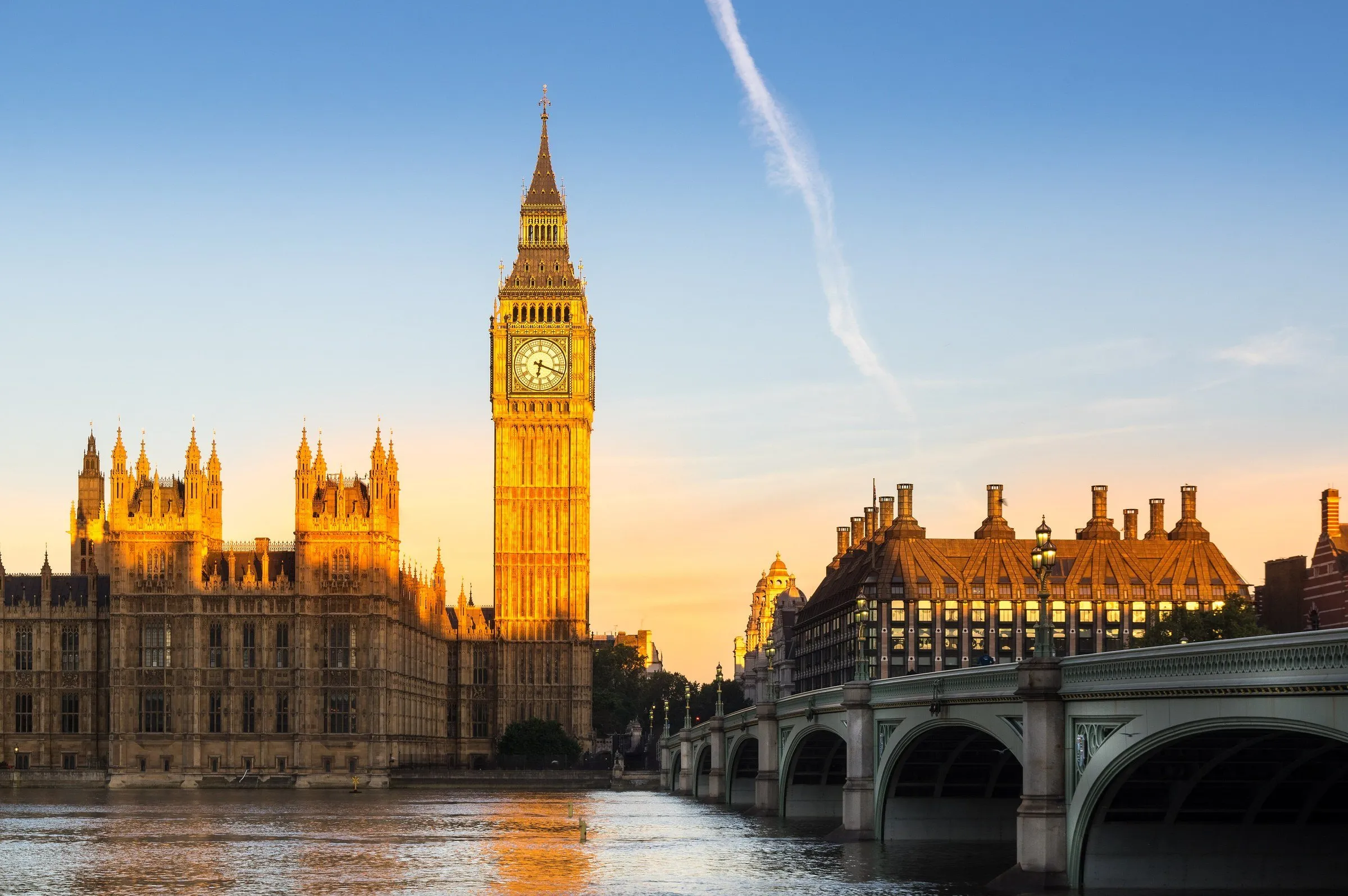 Elizabeth Tower and the Palace of Westminster lit by low morning sun, beside Westminster Bridge and the Thames.