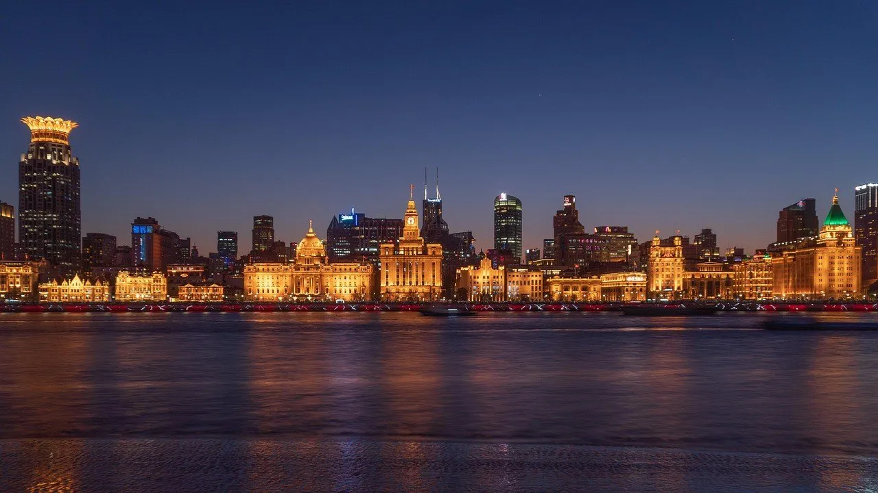 Illuminated historic facades of the Bund seen across the Huangpu under a dark blue sky.
