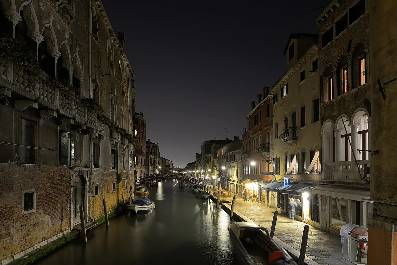 Canal de San Girolamo em Cannaregio à noite, com fachadas, barcos amarrados e luzes refletidas na água.