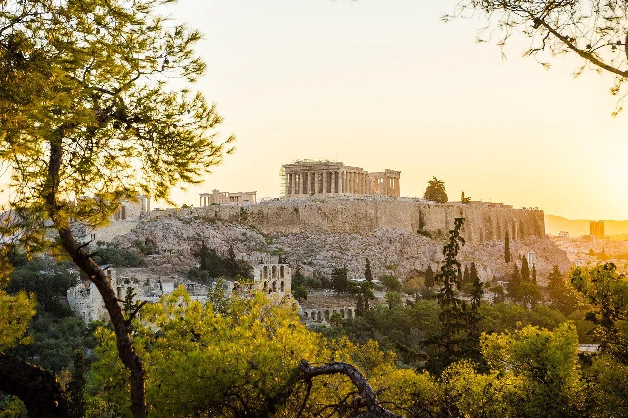 The Acropolis and Parthenon among pine trees, lit by the late afternoon sun in Athens.