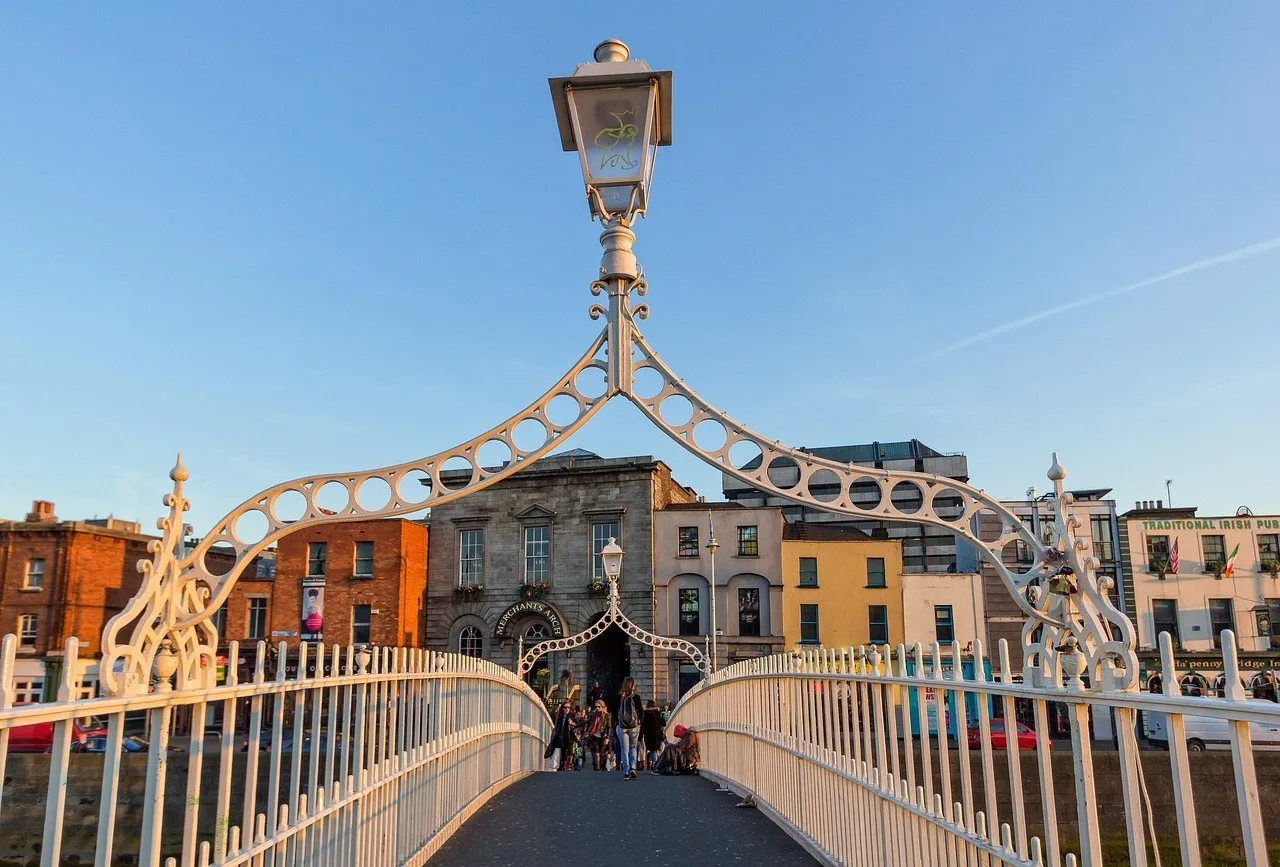 White Ha’penny Bridge with pedestrians and colorful building facades in the background, in Dublin.