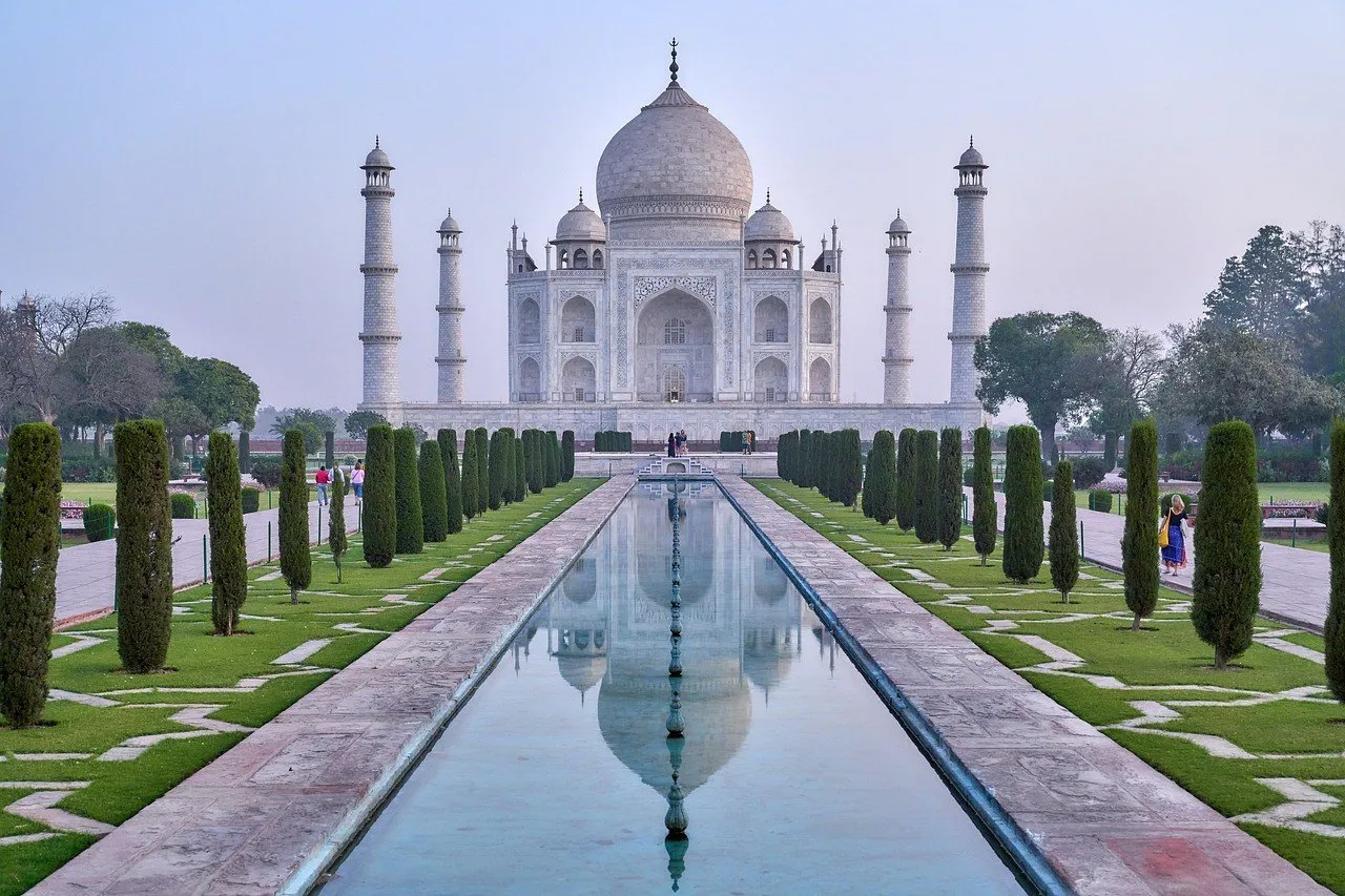 Taj Mahal reflected in the central water channel, between cypresses and garden paths.