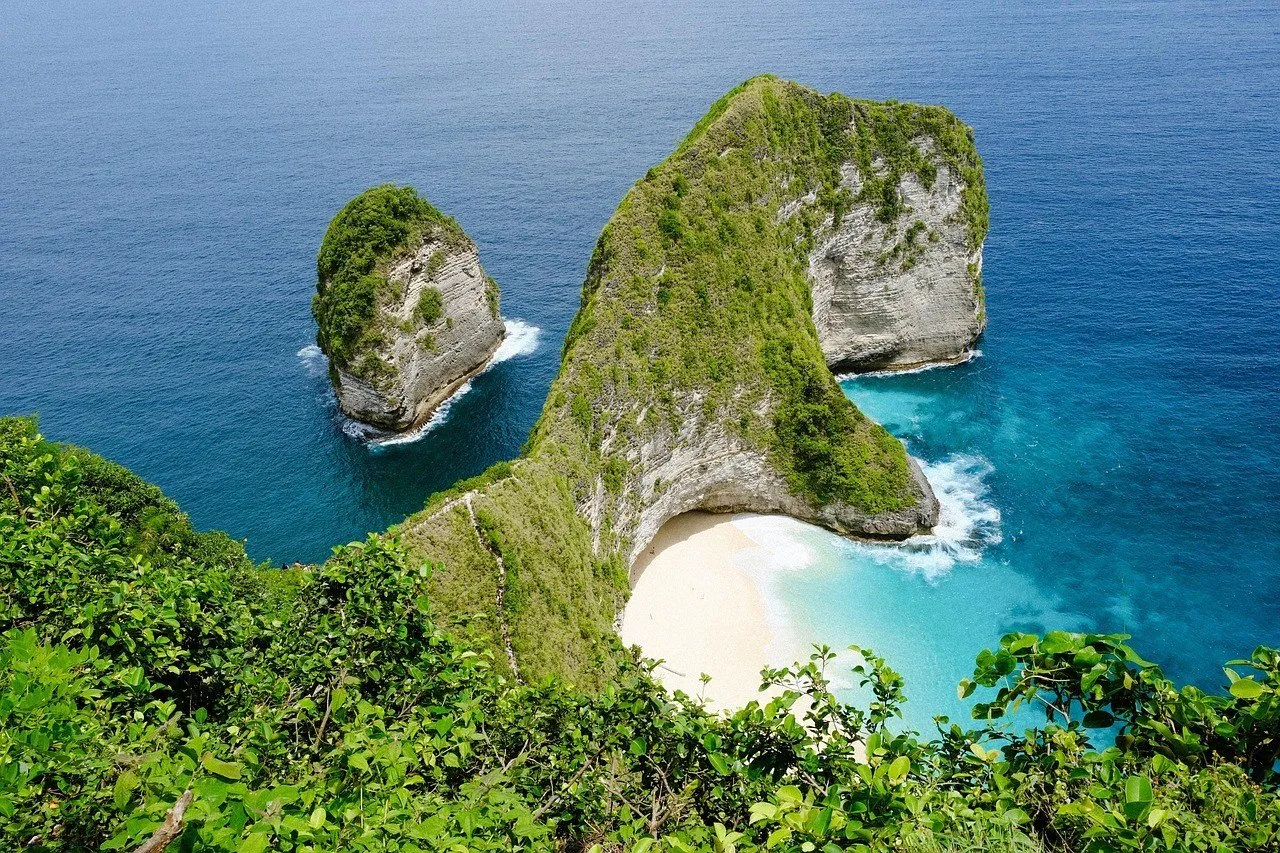 Green Kelingking cliff seen from above, with pale sand, turquoise sea and a rock stack nearby, on Nusa Penida.