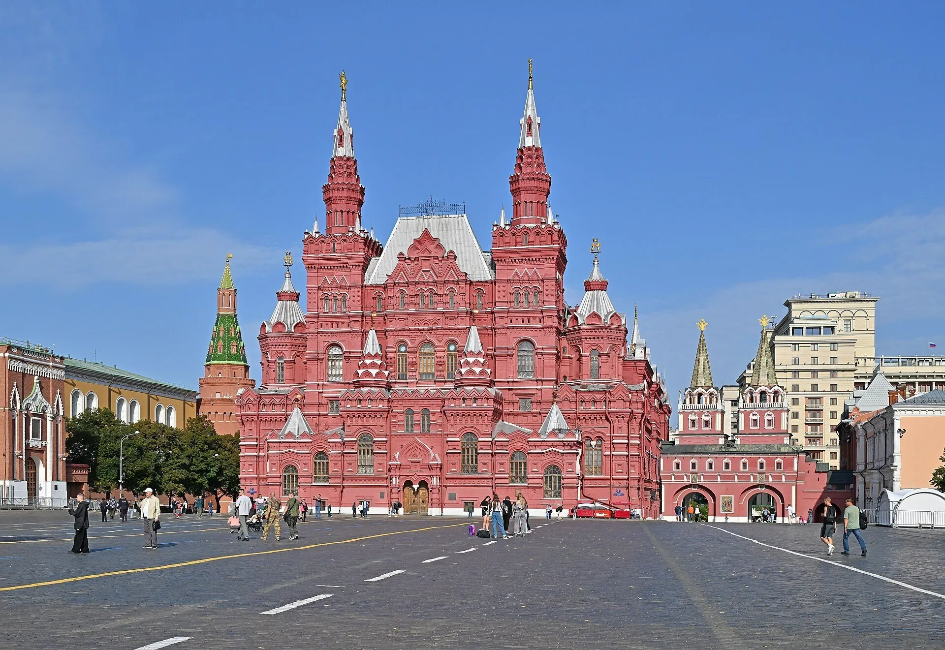 Red facade of the State Historical Museum on Red Square in Moscow, with towers and pedestrians.