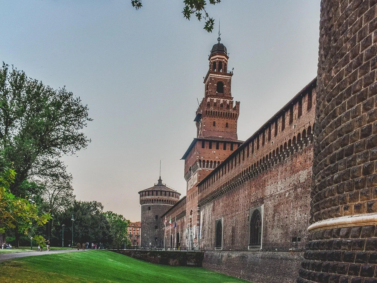 Brick walls of the Sforza Castle in perspective, with the Filarete tower and a lawn at the side.