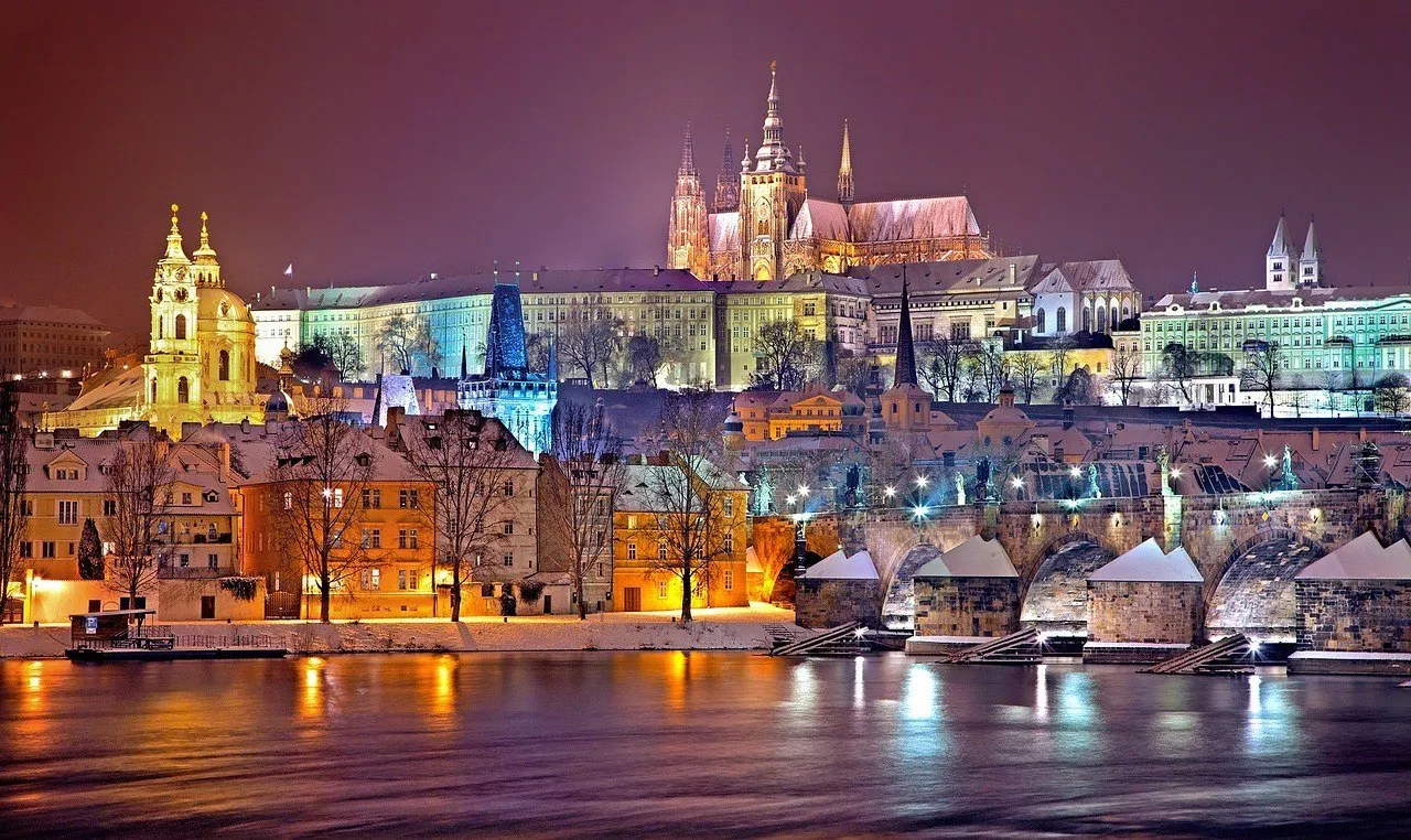 Castillo de Praga y Catedral de San Vito iluminados de noche, con tejados nevados y reflejos en el Moldava.