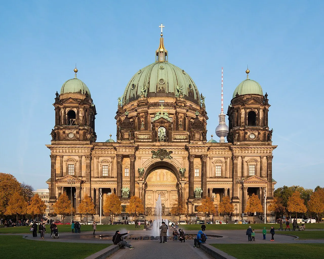 Catedral de Berlim vista de frente, com cúpula verde, fonte e visitantes no Lustgarten.
