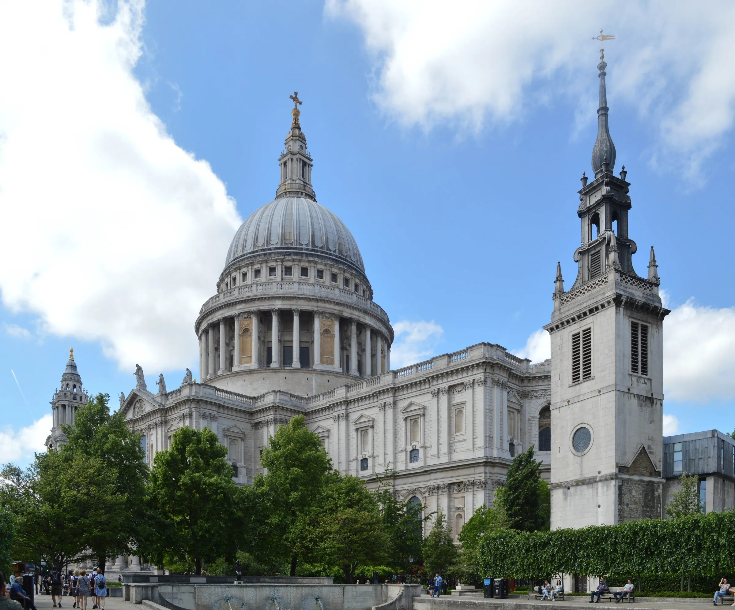 St Paul's Cathedral with its great dome and a side tower, seen through trees under a blue sky with clouds.
