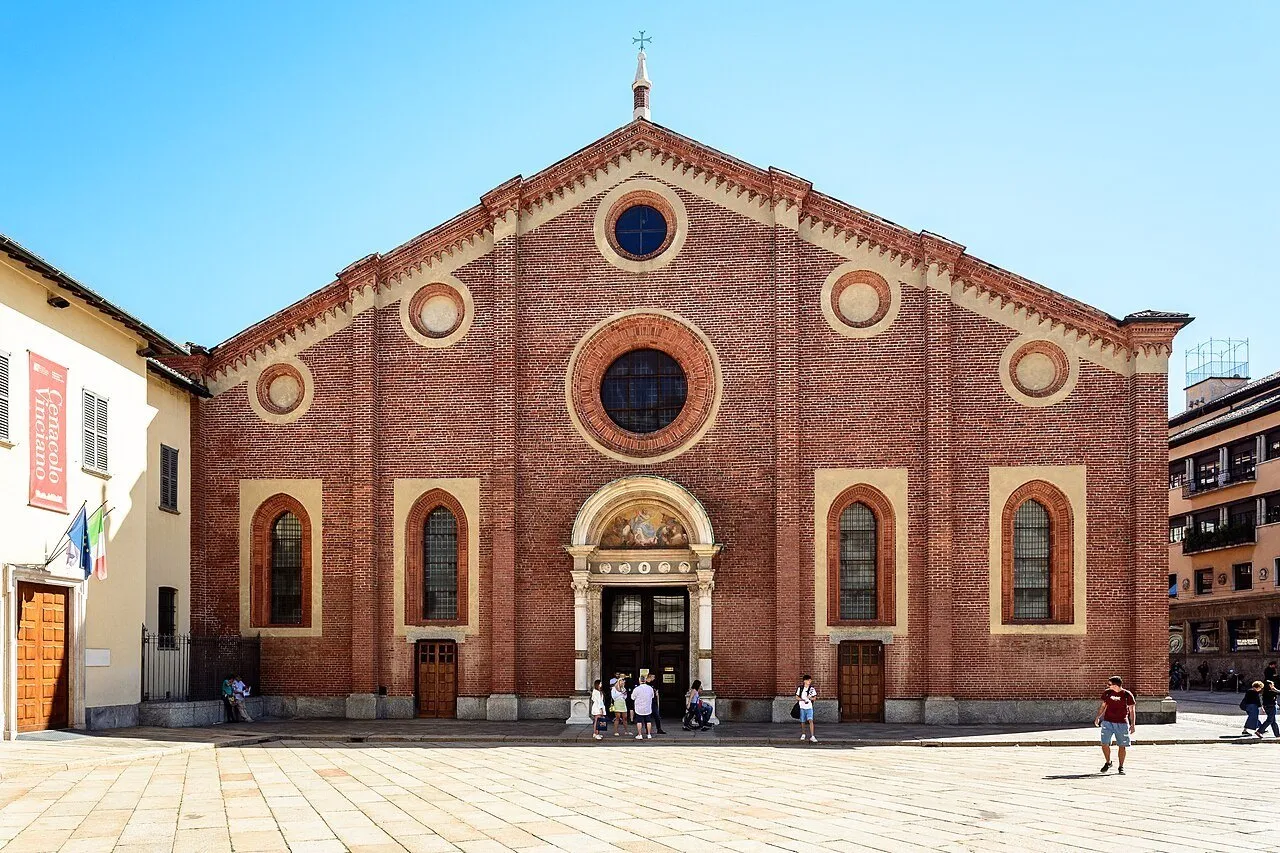 Brick façade of Santa Maria delle Grazie in Milan, with round windows and visitors in the square.