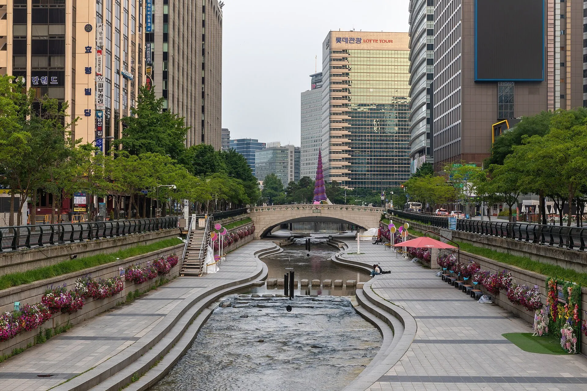 Arroyo Cheonggyecheon entre paseos con flores, un puente de piedra y edificios de Seúl.