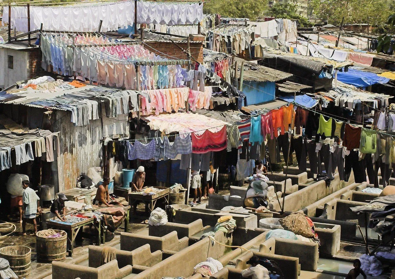 Vista elevada do Dhobi Ghat, em Mumbai, com tanques de concreto, varais cheios de roupas coloridas e trabalhadores ao longe.