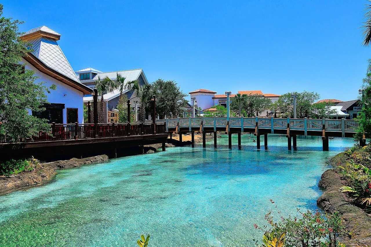 Passarela de madeira e edifícios de Disney Springs sobre um canal de água azul-clara.