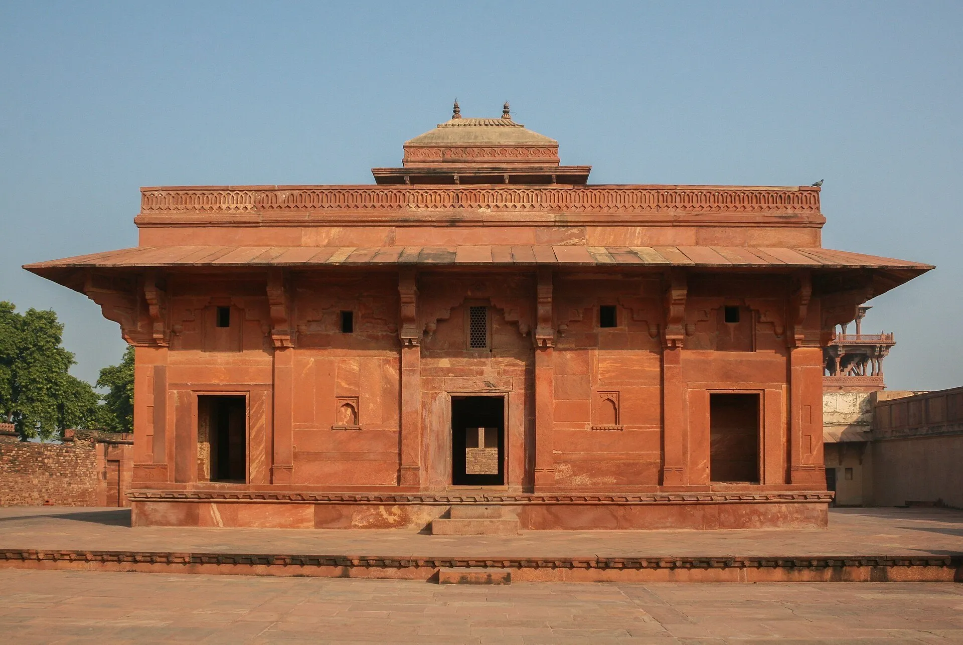 Edificio palaciego de arenisca roja en Fatehpur Sikri, con puertas oscuras y patio sin visitantes.