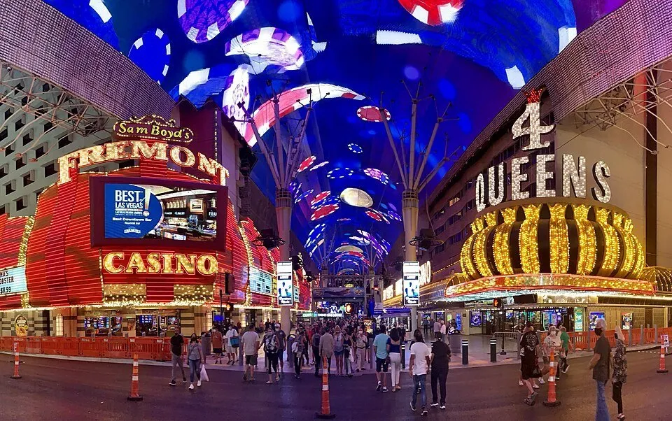 Blue LED canopy over Fremont Street, between the Fremont and Four Queens casino signs, with pedestrians.