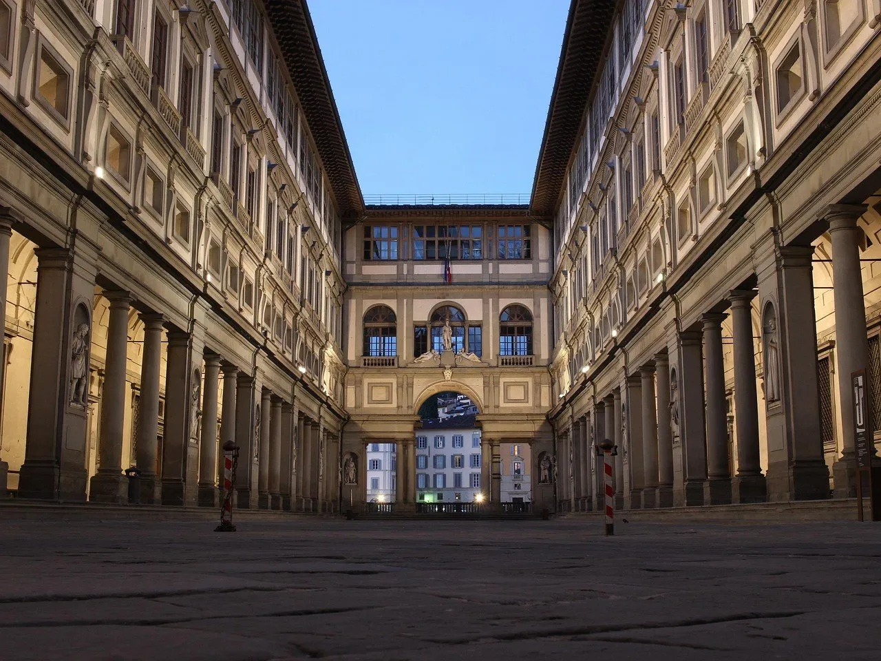 Uffizi courtyard with symmetrical colonnaded wings, lights on and a blue twilight sky.
