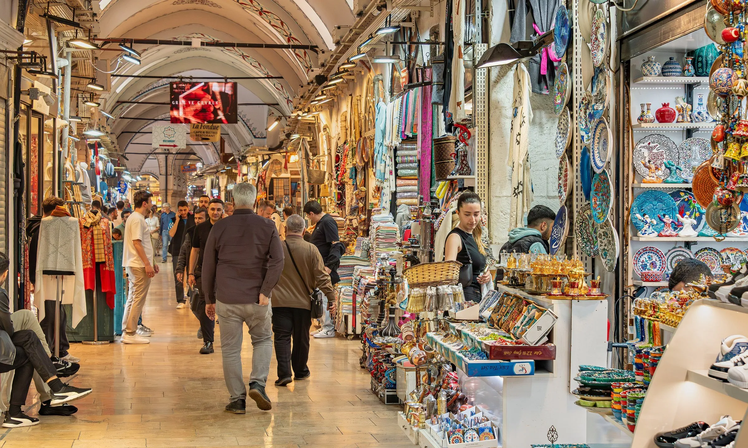 Pasillo abovedado del Gran Bazar de Estambul, con tiendas de cerámica y telas y visitantes caminando por el suelo de piedra.