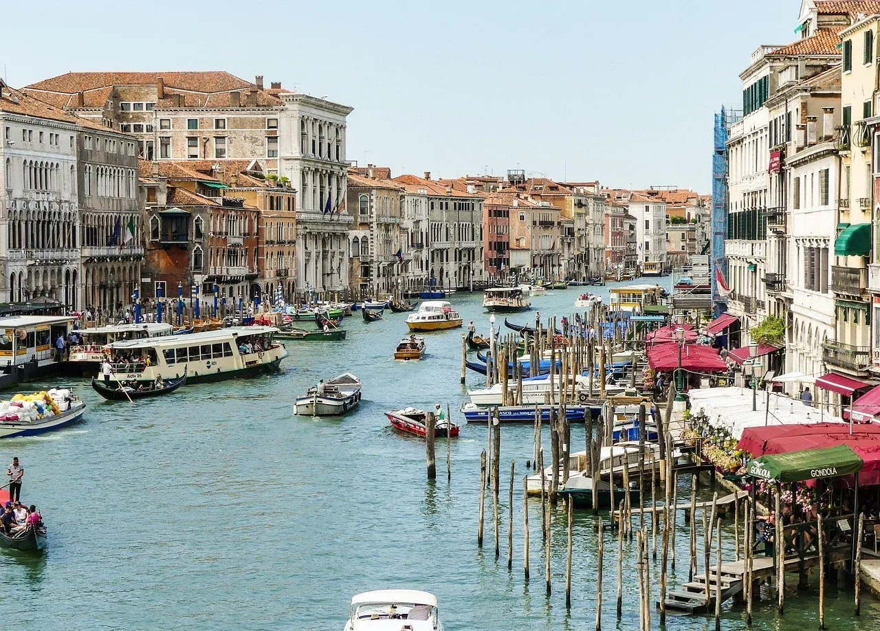 Grande Canal com vaporetto, gôndolas, barcos, píeres e fachadas de palácios nas duas margens.
