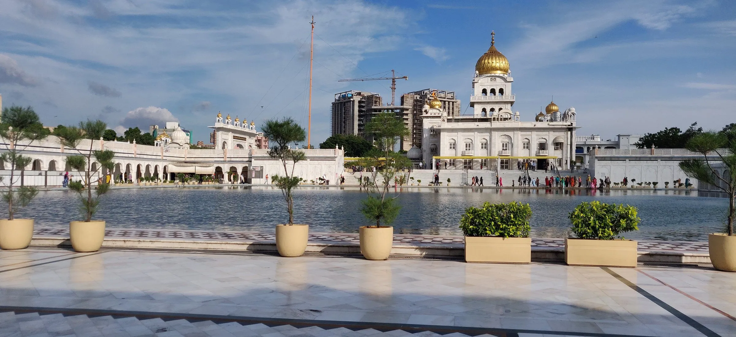 Cúpula dorada del Gurdwara Bangla Sahib tras el lago sagrado, con macetas en el suelo de mármol en primer plano.