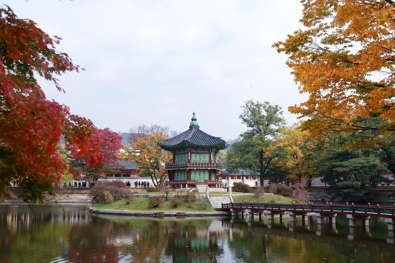 Pabellón de Gyeongbokgung junto a un estanque, rodeado de árboles con hojas de otoño.