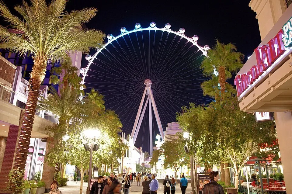 High Roller lit up at night at the end of the LINQ Promenade, among palm trees, shops and pedestrians.