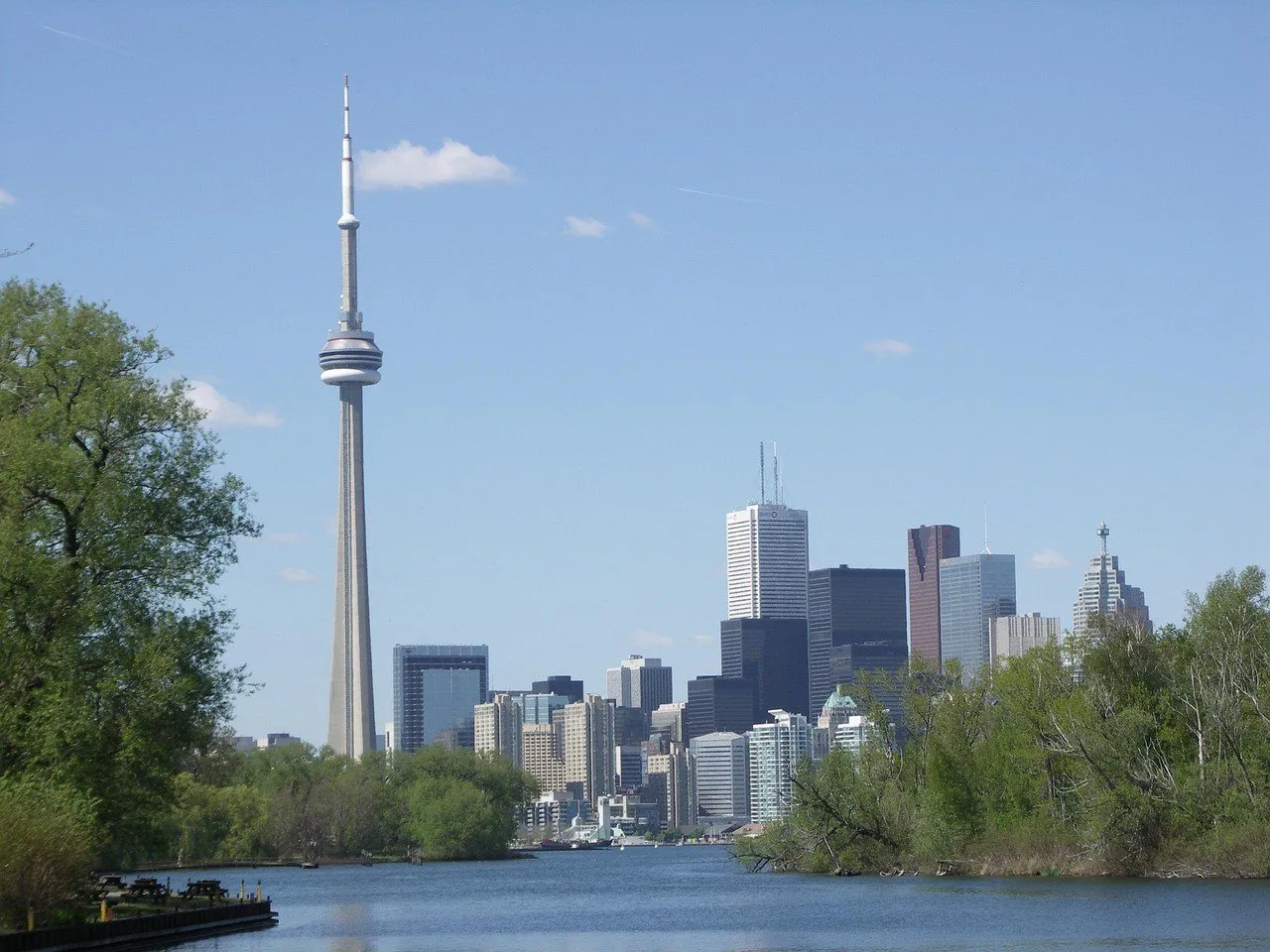 Canal nas Ilhas de Toronto entre árvores verdes, com a Torre CN e os prédios do centro ao fundo.