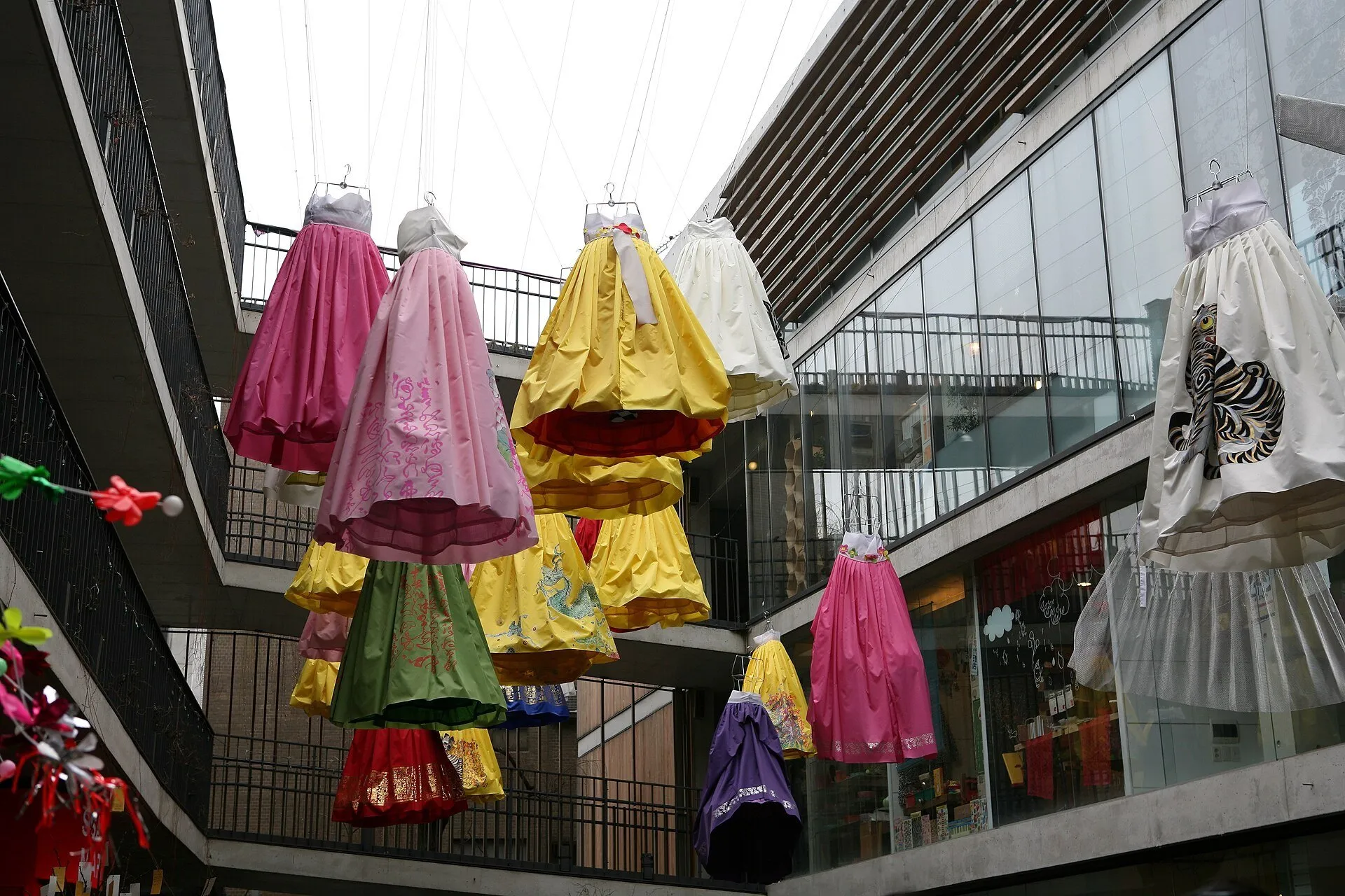 Vestidos de colores colgados sobre un patio comercial en Insadong, con tiendas y pasarelas alrededor.