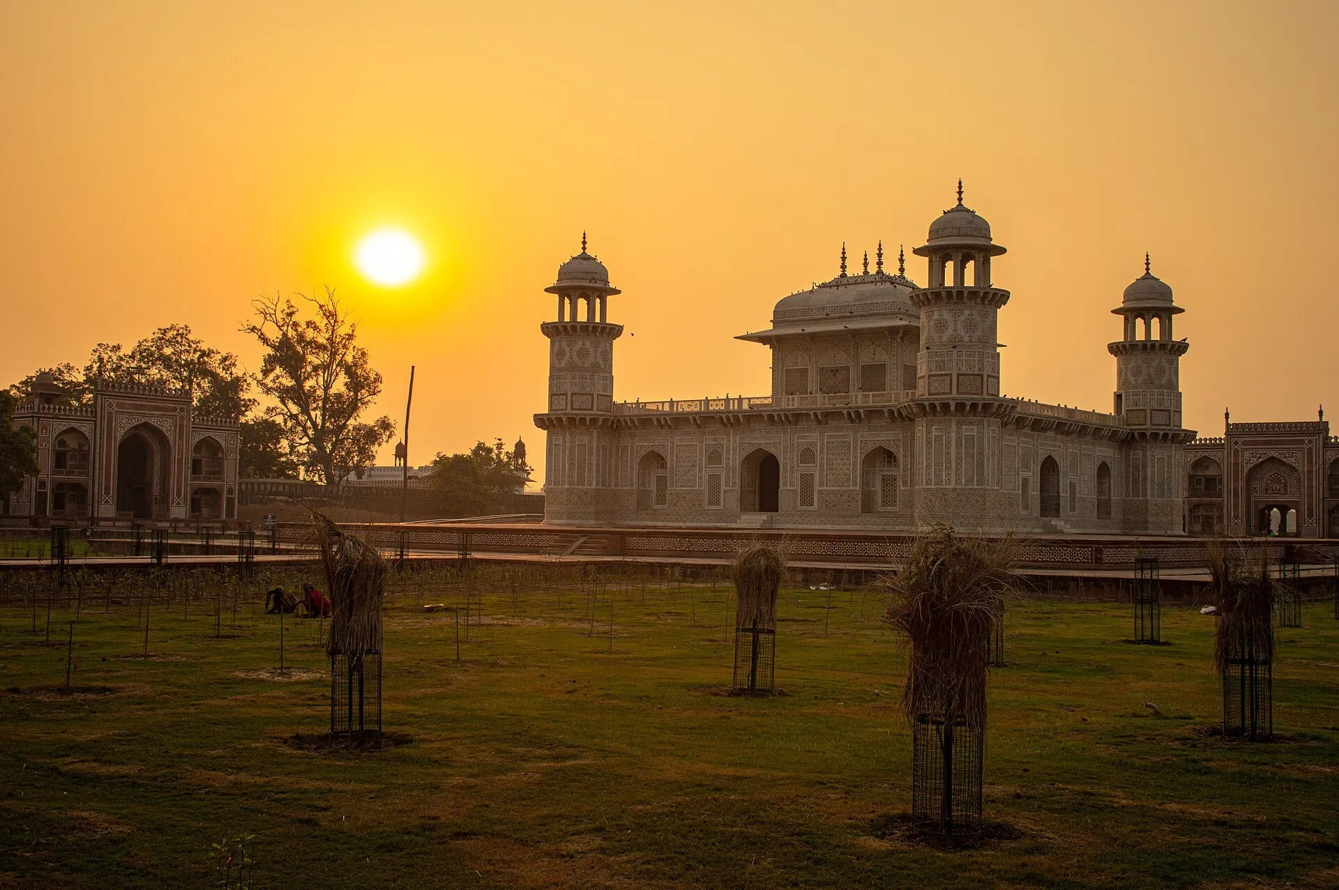 Tumba de Itimad-ud-Daulah y sus torres de esquina ante el sol bajo, con jardín en primer plano.