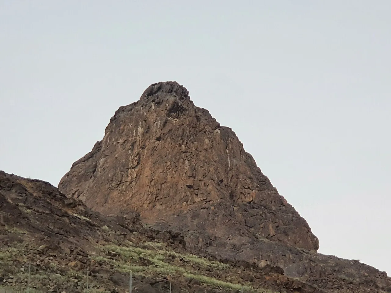 Pico do Jabal al-Nour visto de baixo, com encosta rochosa em primeiro plano e céu claro ao fundo.