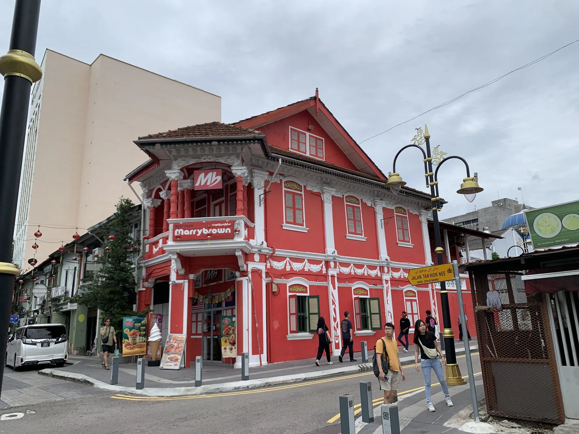 Edifício vermelho e branco de esquina em Jalan Tan Hiok Nee, com pedestres e postes decorativos.