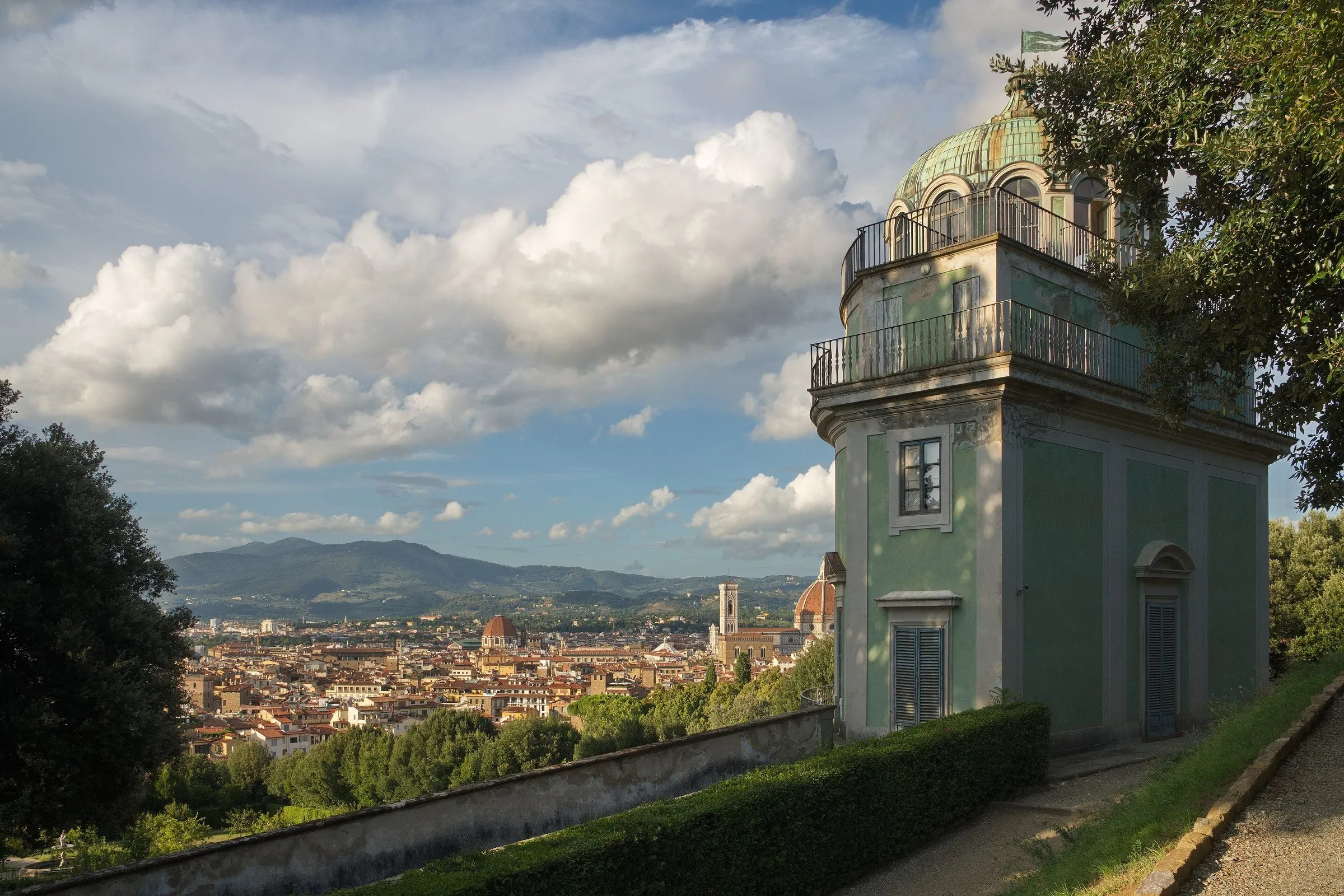 Green pavilion in the Boboli Gardens, with hedges, trees and a Florence panorama behind.