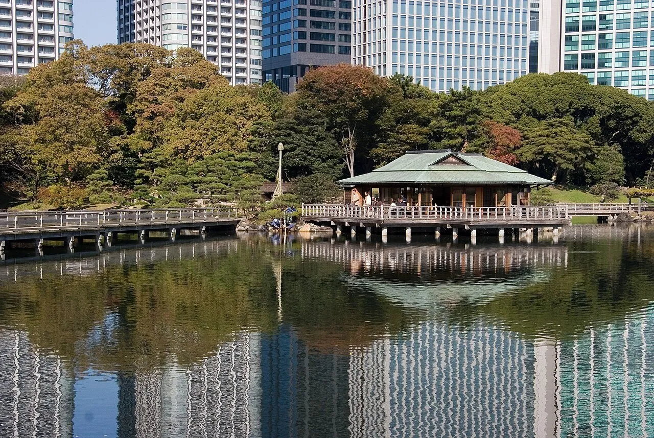 Casa de té sobre el estanque de Hamarikyu, con árboles y rascacielos de Shiodome reflejados en el agua.