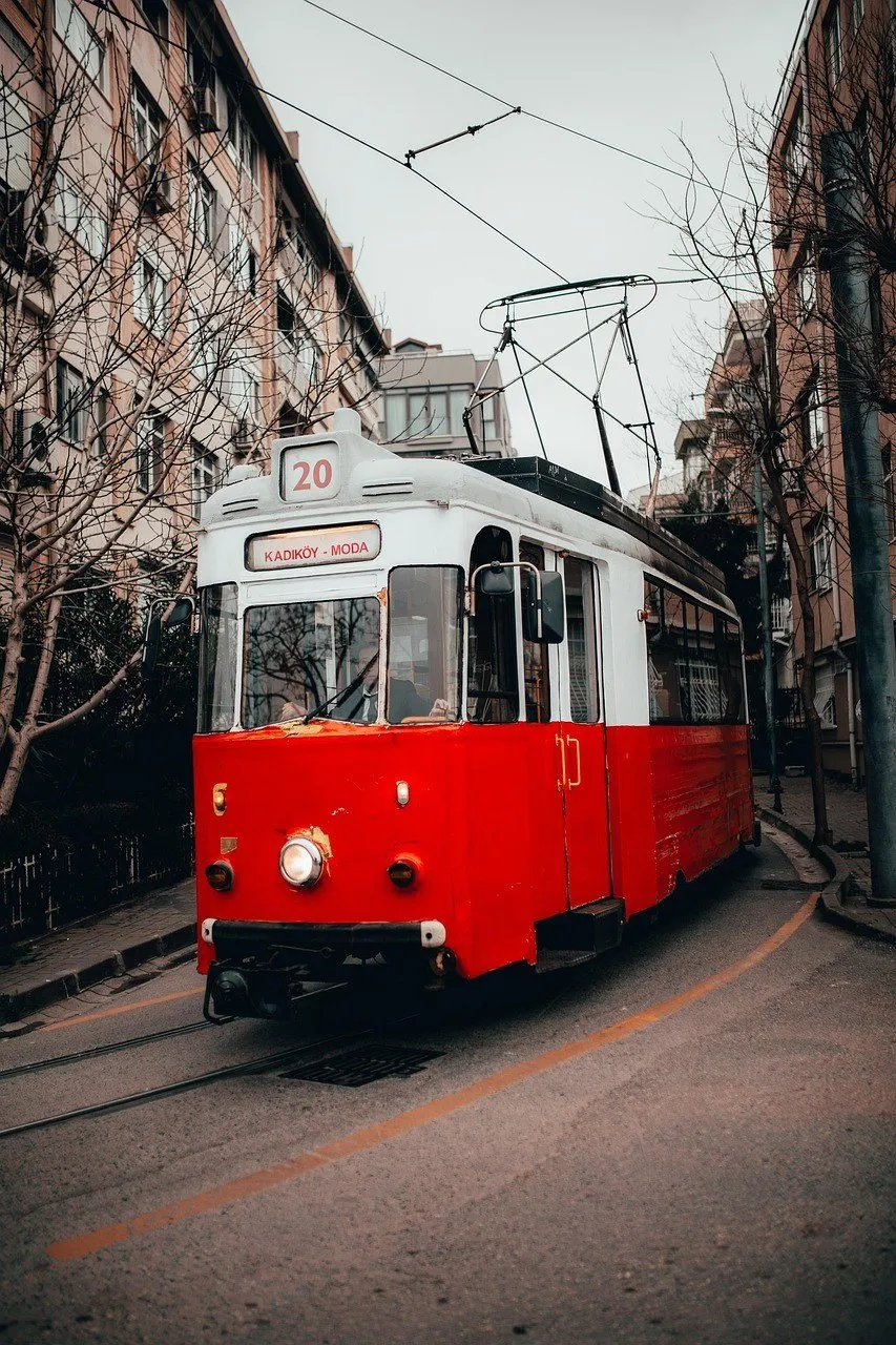 Tranvía rojo y blanco con el cartel Kadıköy–Moda en una calle del barrio, entre edificios y árboles sin hojas.