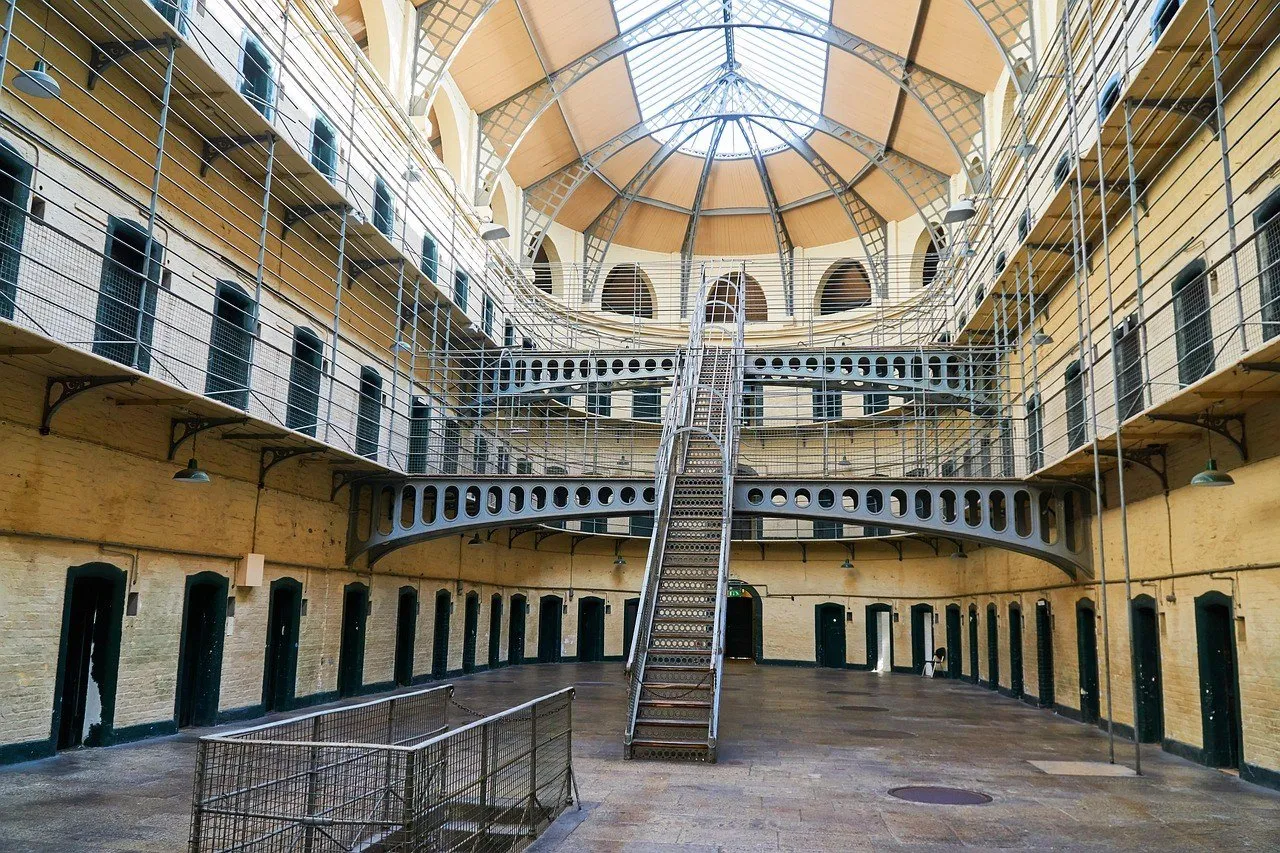 Salón de Kilmainham Gaol con escalera central, pasarelas metálicas, puertas de celdas y techo acristalado.