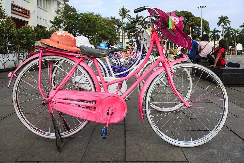 Fila de bicicletas coloridas, com uma rosa em primeiro plano, na praça Fatahillah em Kota Tua.