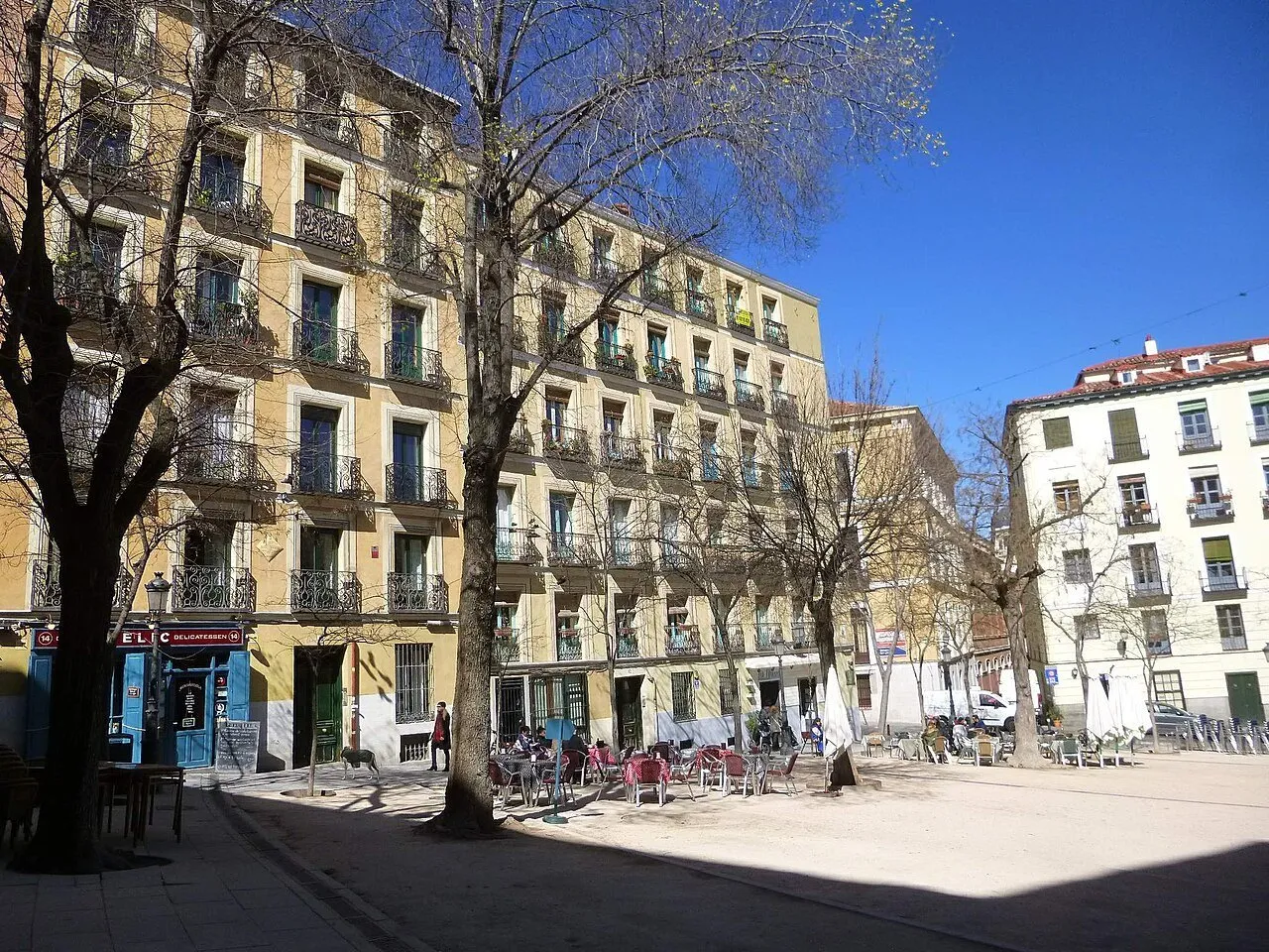 Plaza de la Paja in La Latina, with trees, yellow and white facades and outdoor tables.