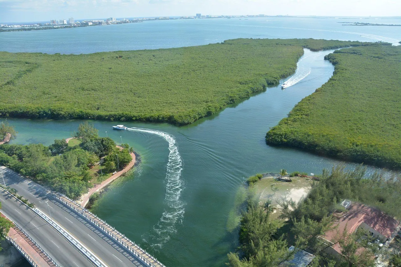 Vista elevada de canais entre manguezais da Nichupté, com lanchas, ponte e hotéis distantes.