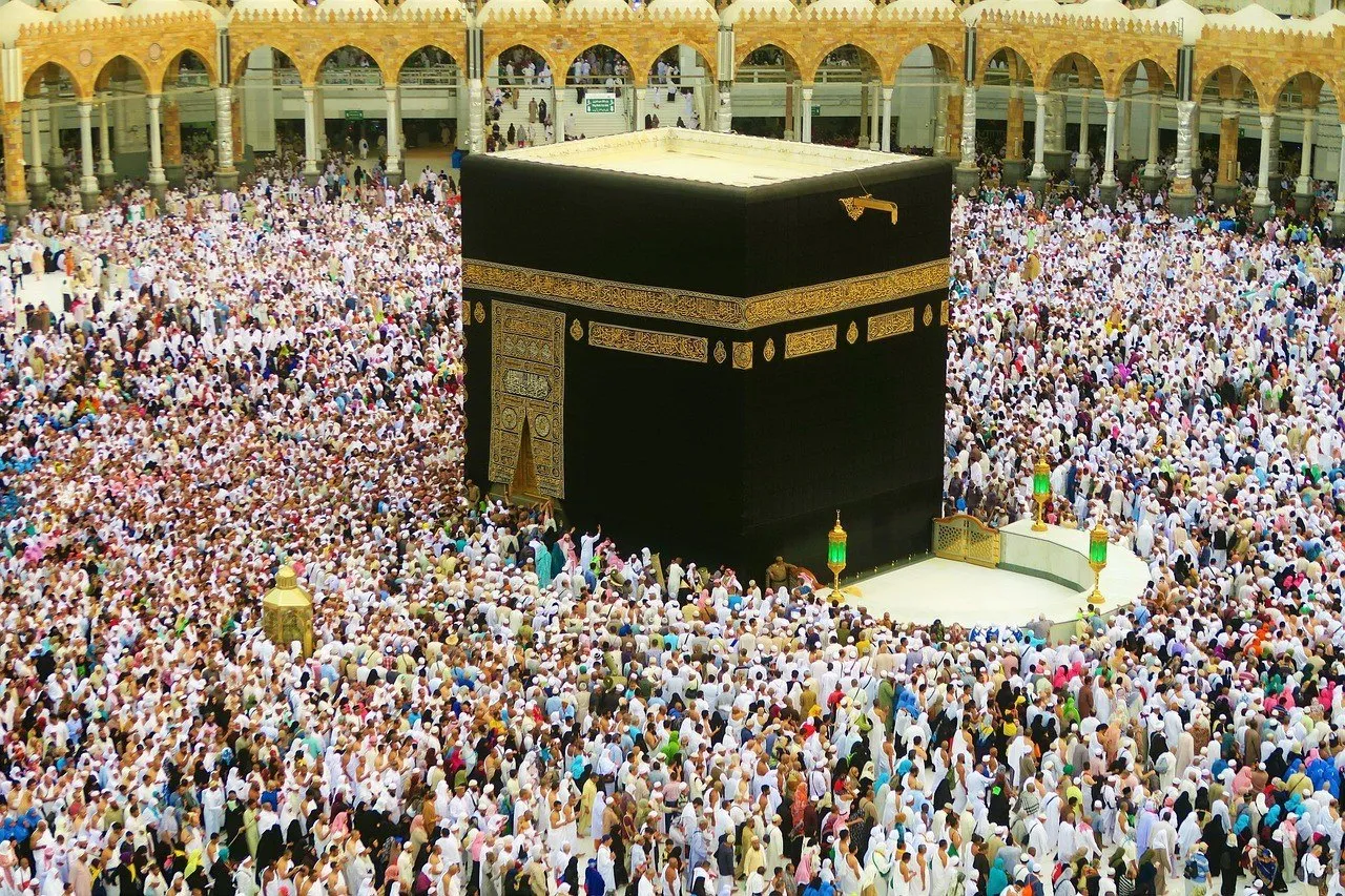 Kaaba vista de cima, com tecido preto e bordados dourados, arcadas e peregrinos ao redor.