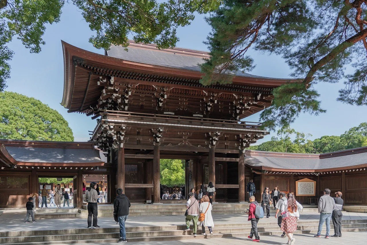 Puerta de madera del Meiji Jingu, con árboles y visitantes en el patio a la luz del día.
