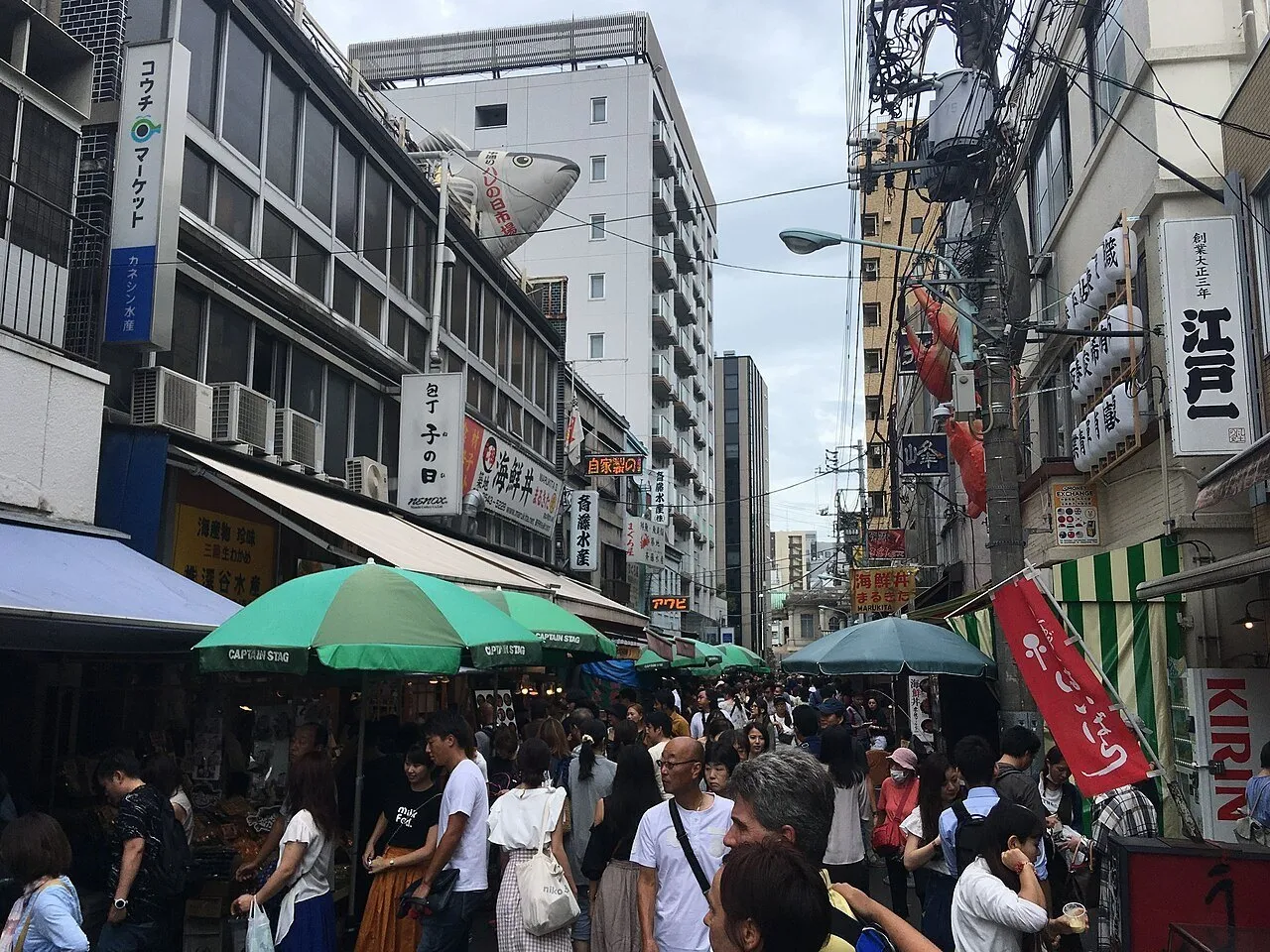 Calle del Mercado Exterior de Tsukiji con puestos bajo sombrillas verdes, letreros y muchos visitantes.