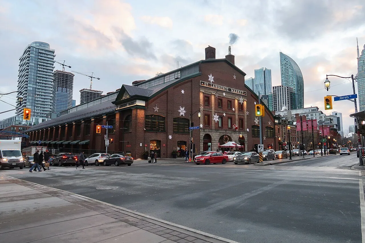 Fachada de tijolos do St. Lawrence South Market, com decoração de inverno, carros e prédios ao fundo.
